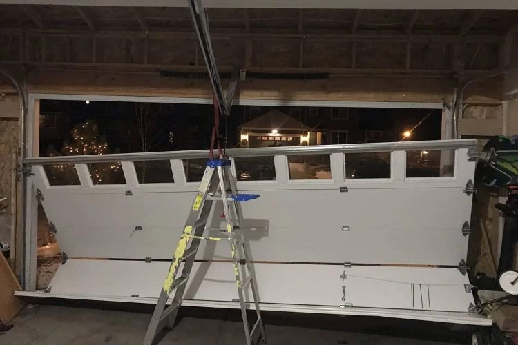 Sectional garage door lifted clear of its tracks and propped on a stepladder inside the garage during a night call, the open doorway and the dark street beyond