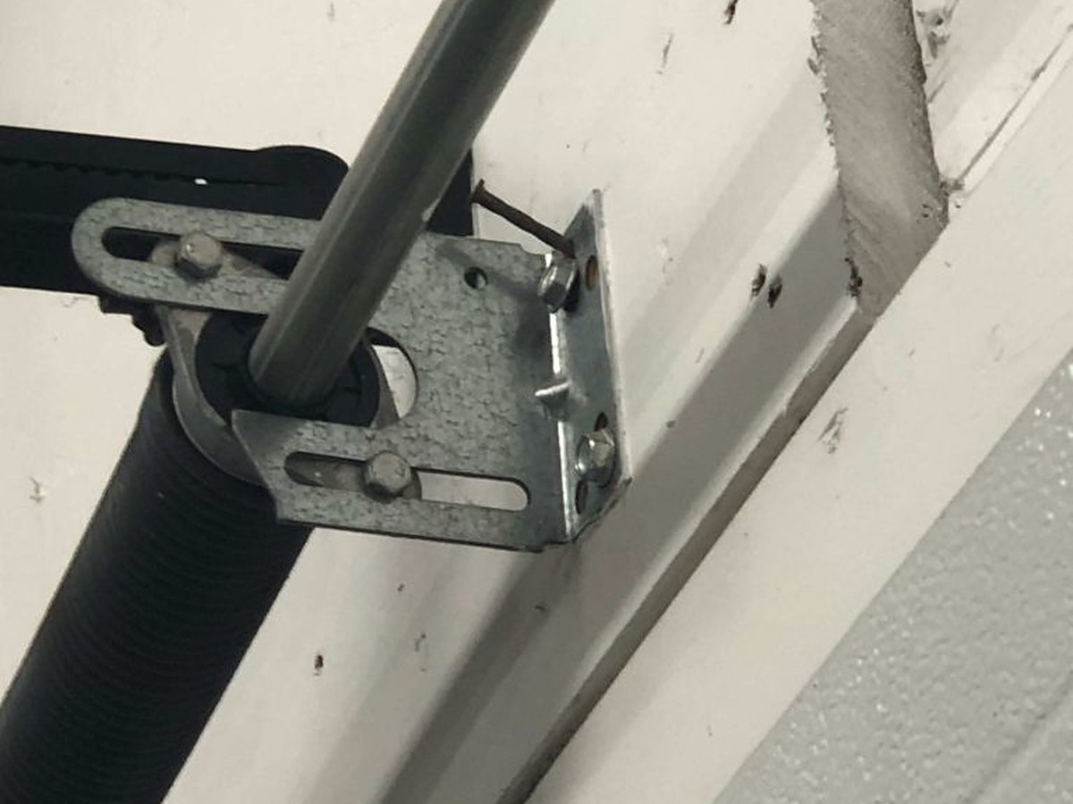 Centre bearing plate carrying the torsion shaft, bolted to the header above a garage door, with the spring end fitting alongside