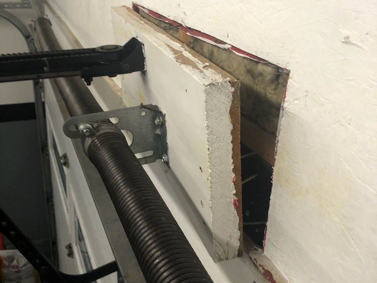Header wall opened up beside a torsion spring so the structural backing behind the anchor bracket can be reached